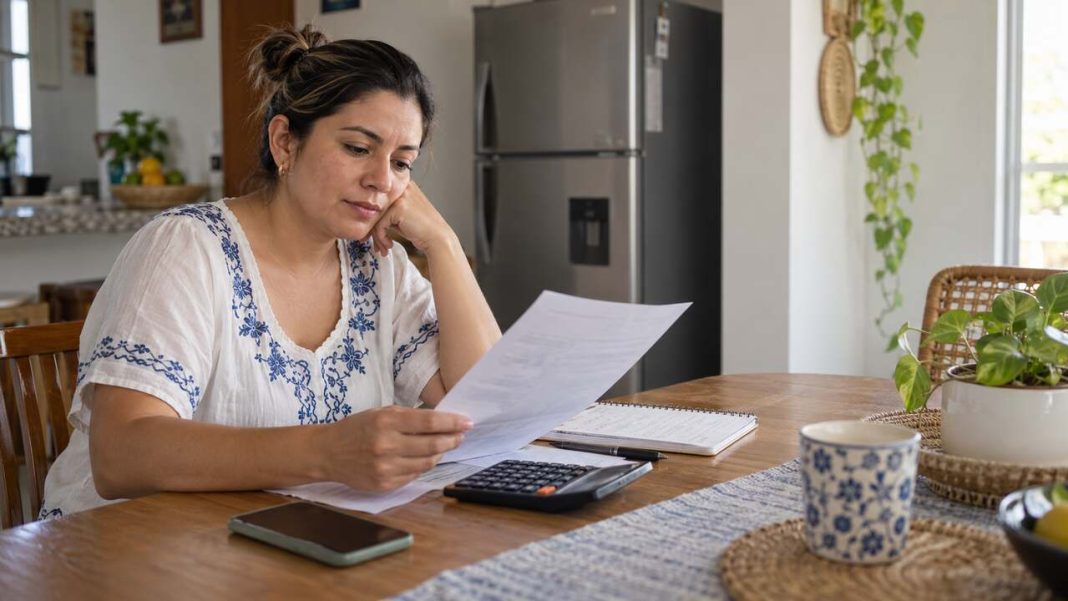Mujer revisa un extracto y su presupuesto doméstico junto a una calculadora.